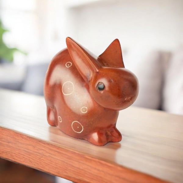 A brown stone carved bunny figurine on a wooden shelf
