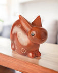 A brown stone carved bunny figurine on a wooden shelf