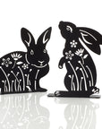 Two metal silhouettes of rabbits with floral designs, one sitting and one standing, against a white background.
