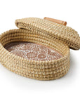 A terracotta bread warmer with a butterfly garden design, consisting of a stone incised with a pattern, placed inside a woven grass basket with a palm wrap detail, accompanied by a lid.