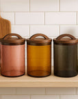 Three glass canisters with wooden lids on a kitchen shelf.