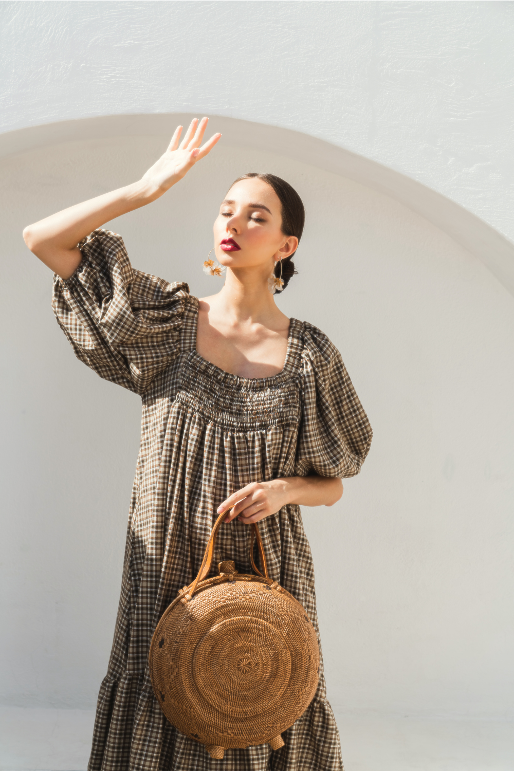 A woman holding an oversized rattan round satchel with leather handles and a natural brown color.