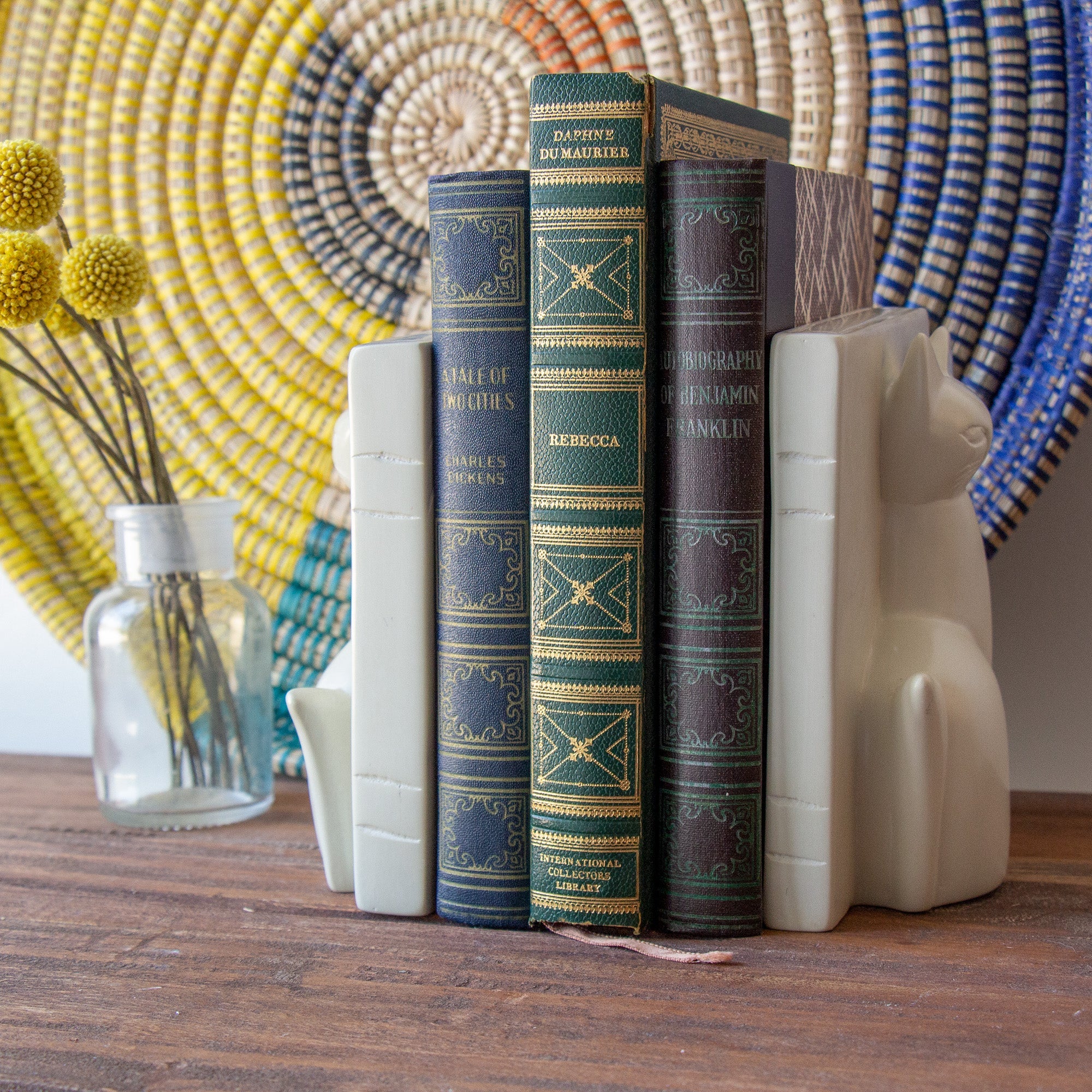 Two carved stone cat bookends holding three books together on a wooden table