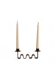 A black metal candle holder with a wavy design, holding two taper candles against a white background.