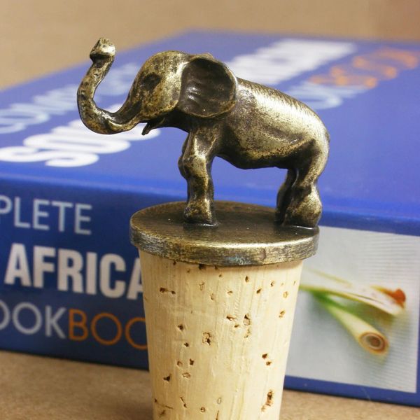 A brass elephan wine bottle stoppers sitting atop corks standing upright on top of a wooden table in front of a book.