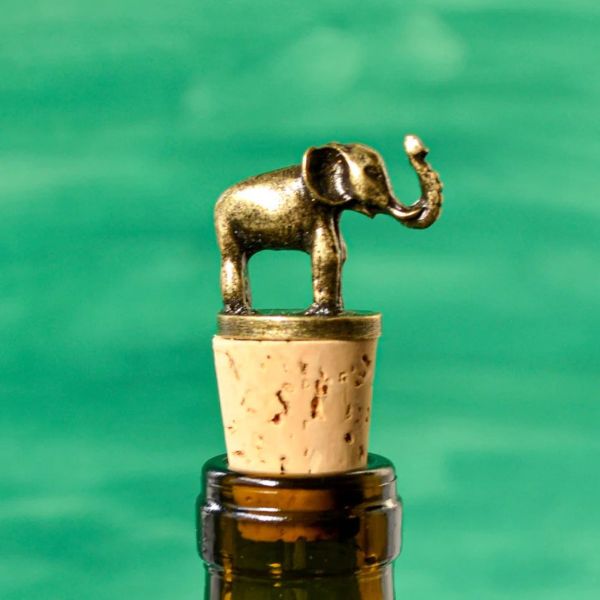 A brass elephant wine bottle stopper sitting atop corks on a bottle of wine.