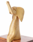 A wooden elephant sculpture perched on a ledge, with a subtle wood grain finish
