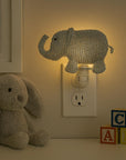 Decorative elephant night light on a wall with a teddy bear and alphabet blocks in the foreground.