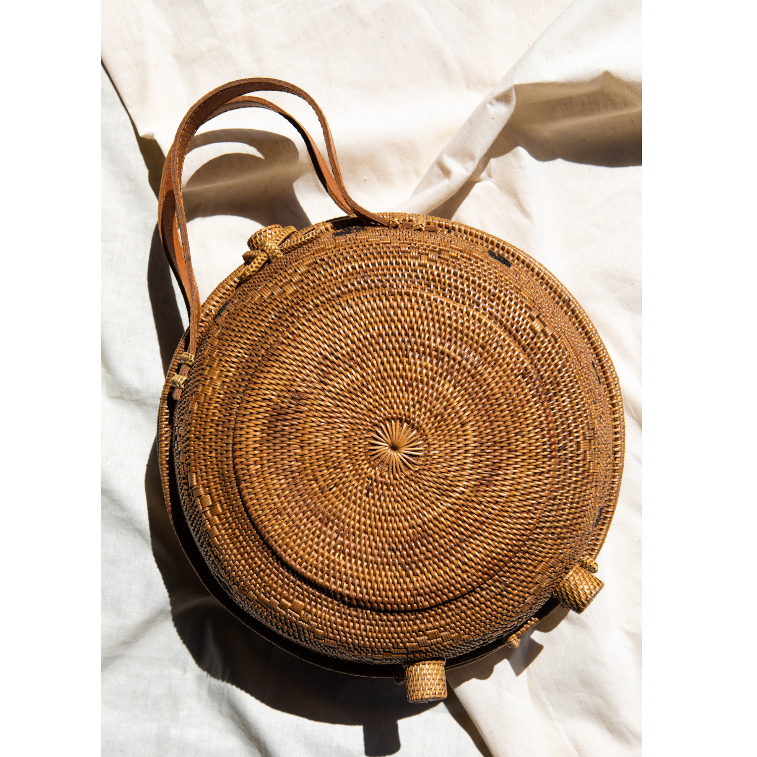 An oversized rattan round satchel with leather handles and a natural brown color.