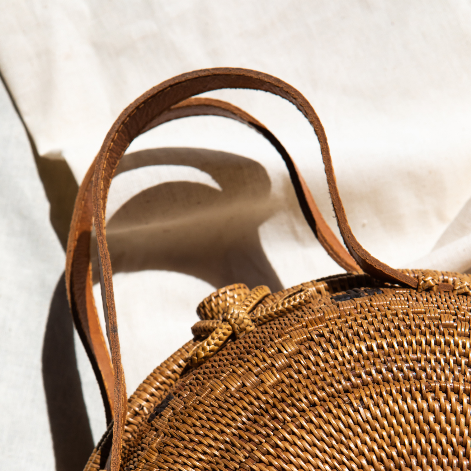 An oversized rattan round satchel zoomed in on the leather handles with a natural brown color.