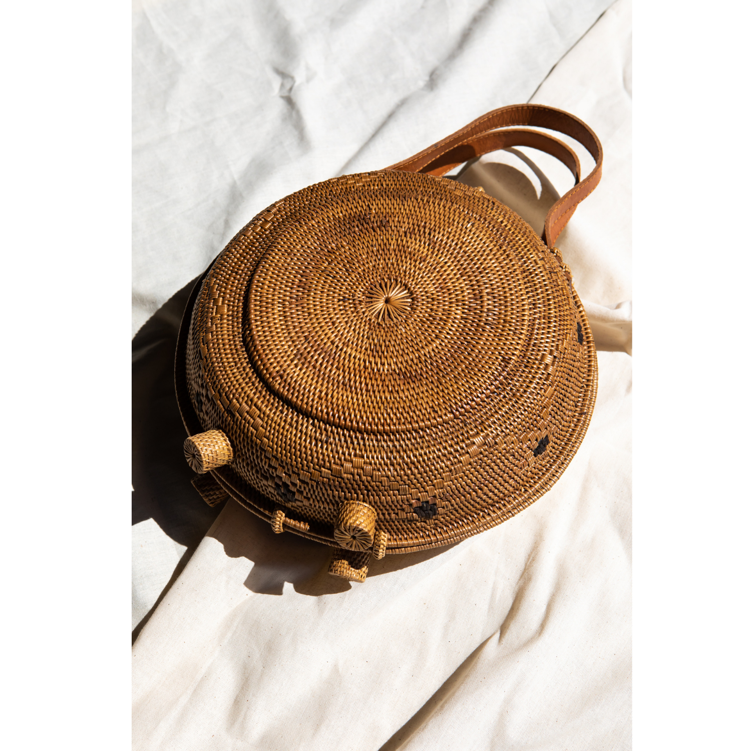 An oversized rattan round satchel with leather handles and a natural brown color with a gray background.