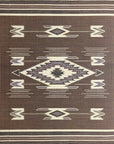 A rectangular rug with a traditional Navajo geometric motif design in earth tones, featuring a central diamond shape with border patterns.