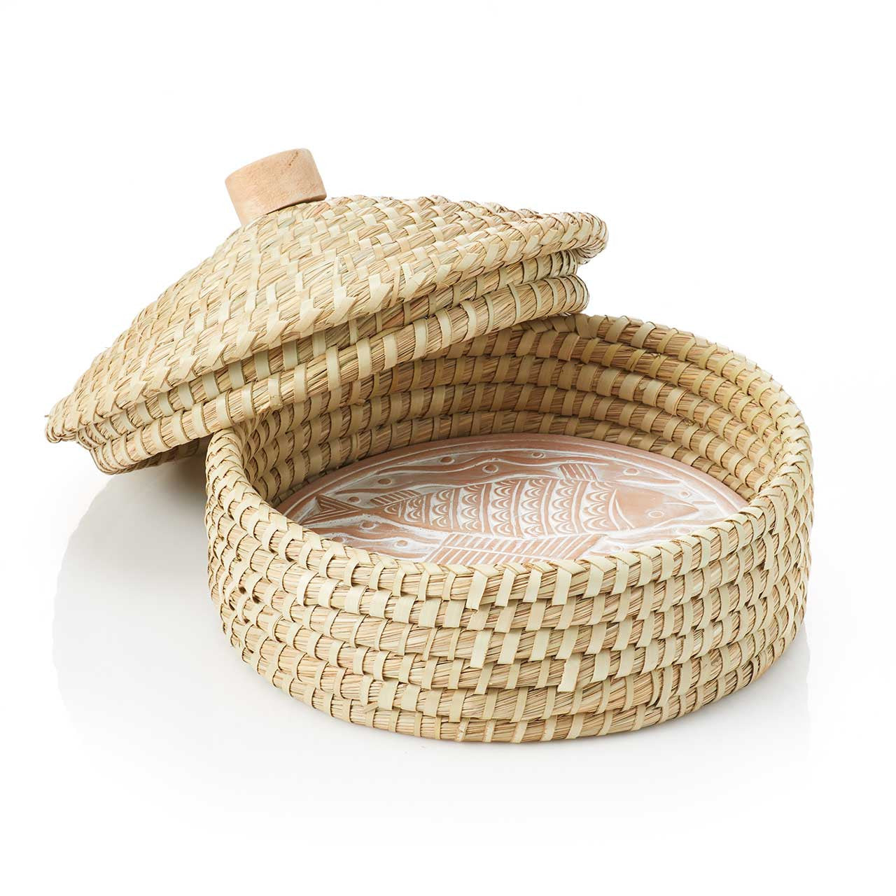 A terracotta bread warmer with a nautical-inspired macha design, featuring a lid and placed within a handwoven grass basket with palm wrap detail.