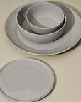 A set of gray dinnerware including one large plate, one medium plate, one large bowl, and one medium bowl, all with a wide rim