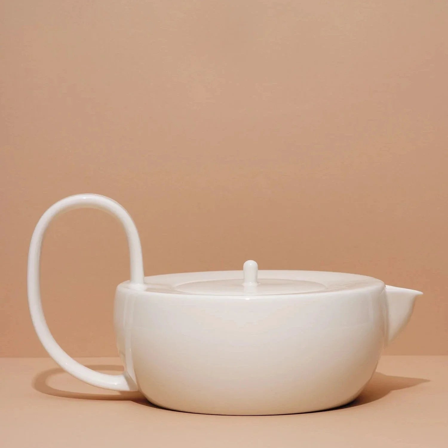 A white ceramic teapot with a simple, modern design against a beige background