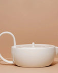 A white ceramic teapot with a simple, modern design against a beige background
