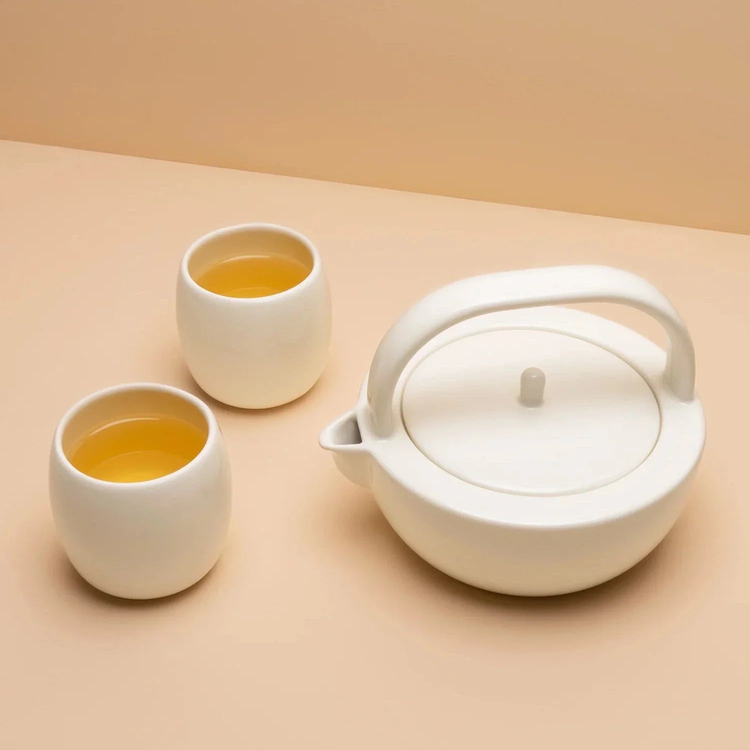 A small white ceramic teapot set with two matching cups, presented on a two-tone background