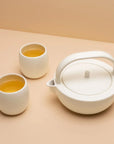 A small white ceramic teapot set with two matching cups, presented on a two-tone background