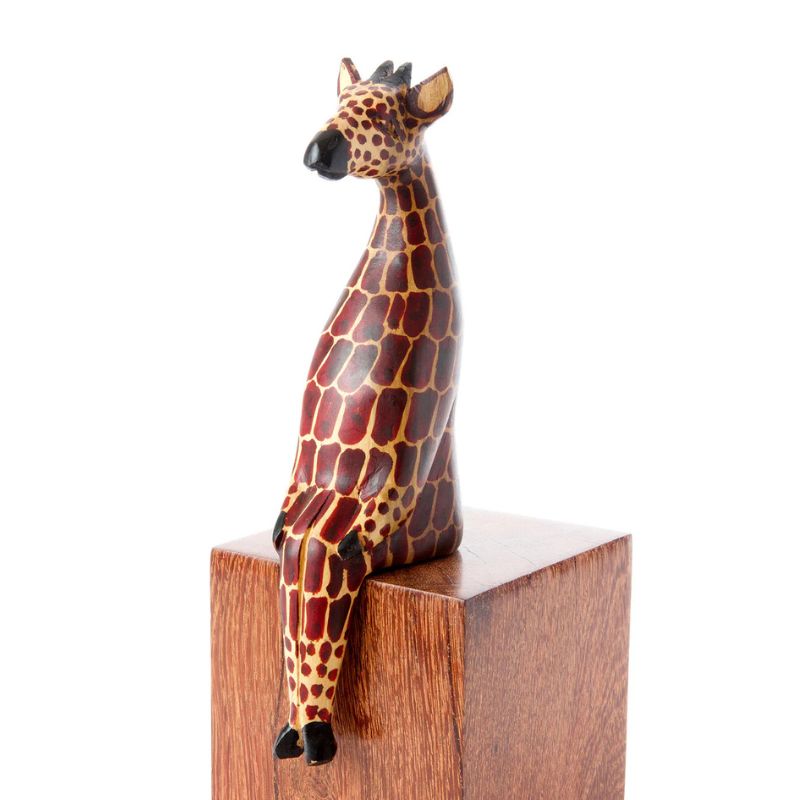 A handcrafted wooden giraffe shelf sitter with hand painted spots, perched on a wooden ledge.