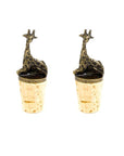 A set of two brass giraffe-shaped wine bottle stoppers sitting atop corks.