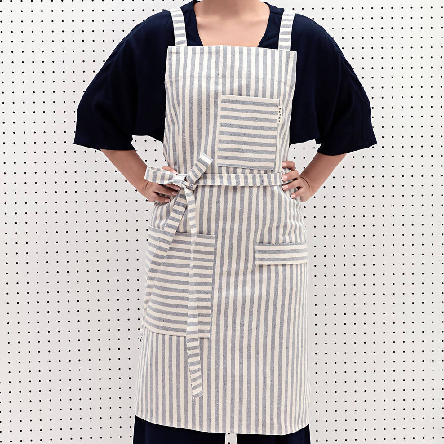 A person wearing a striped crossback bib apron with multiple pockets and a utility loop.