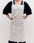 A person wearing a striped crossback bib apron with multiple pockets and a utility loop.