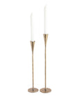Two tall brass candle holders with white candles on a white background