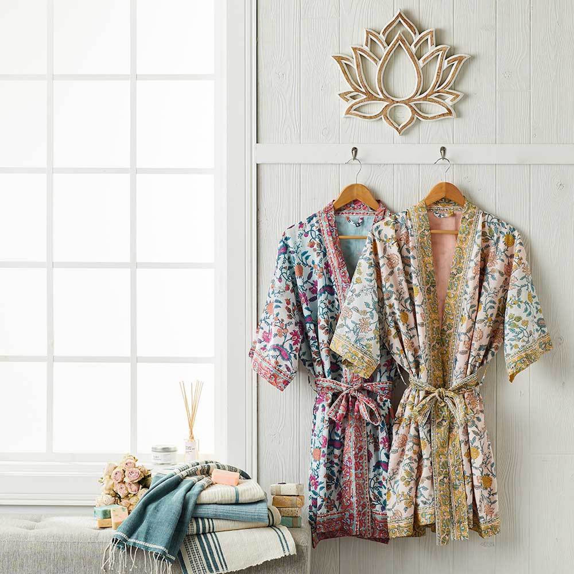 A handmade wooden lotus wall art piece hanging on a wall above two bathrobes