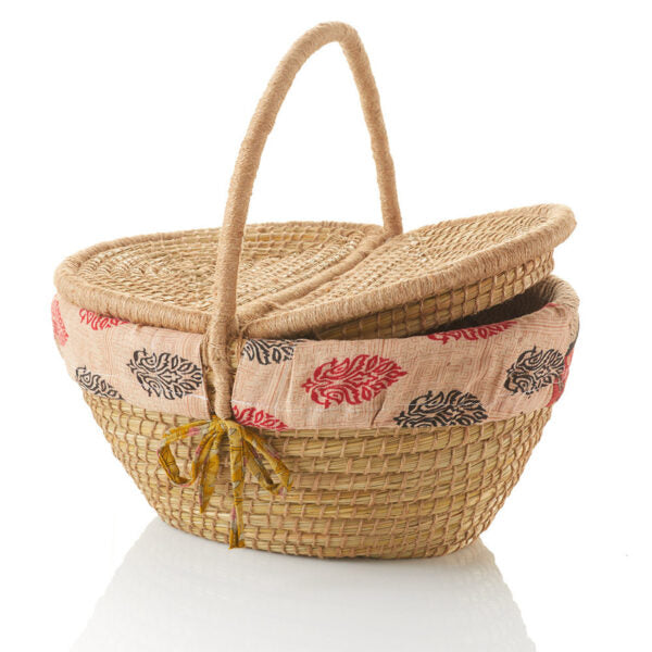 An oval-shaped kaisa grass and jute picnic basket with a handle and two flaps displayed against a white background