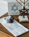 Decorative items including a Menorah, dreidels on a tea towel, and a Star of David card on a wooden surface