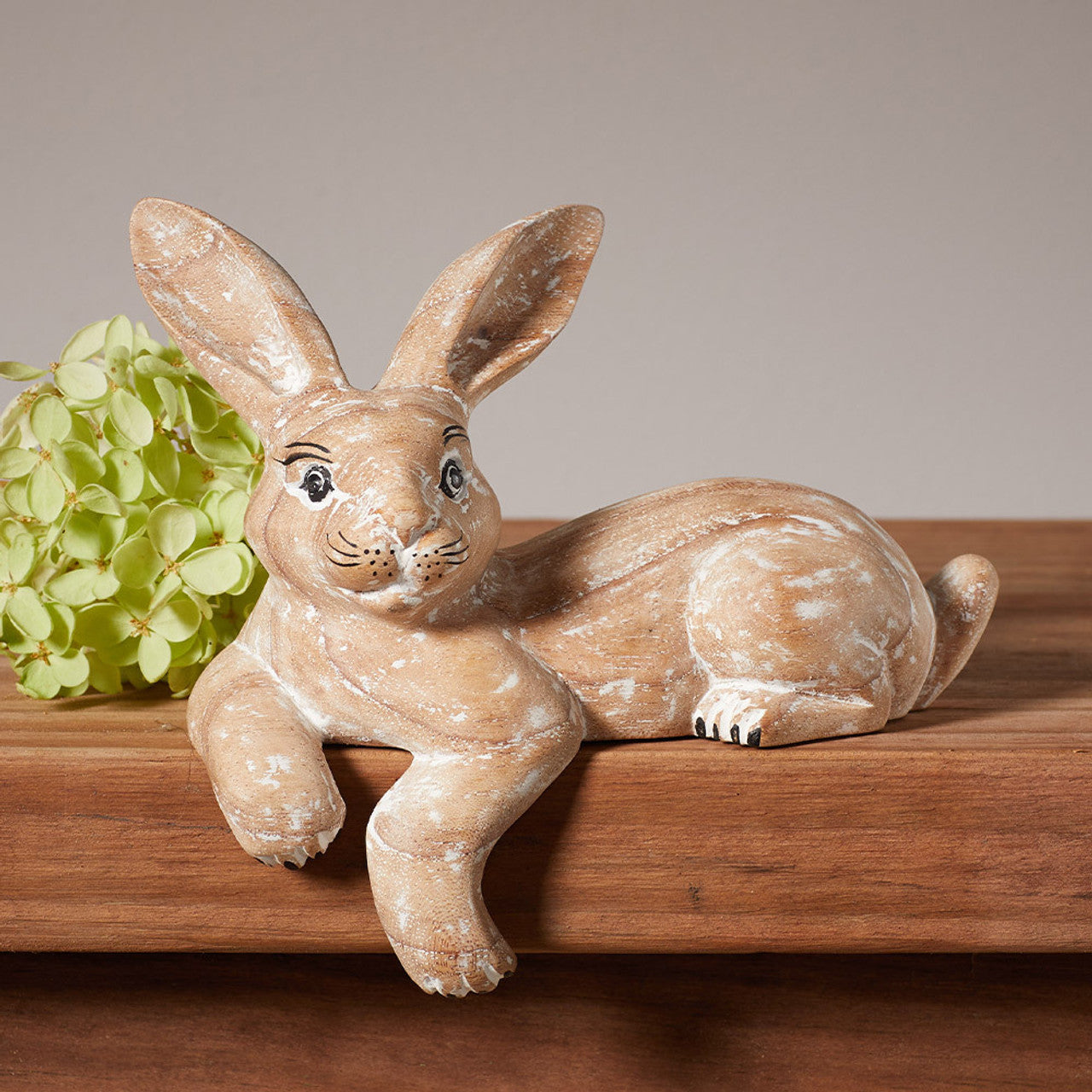 A handmade whitewashed wooden hare shelf sitter sitting on a wooden shelf