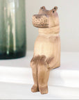 Wooden hippo figurine on a shelf ledge with a blurred green container in the background