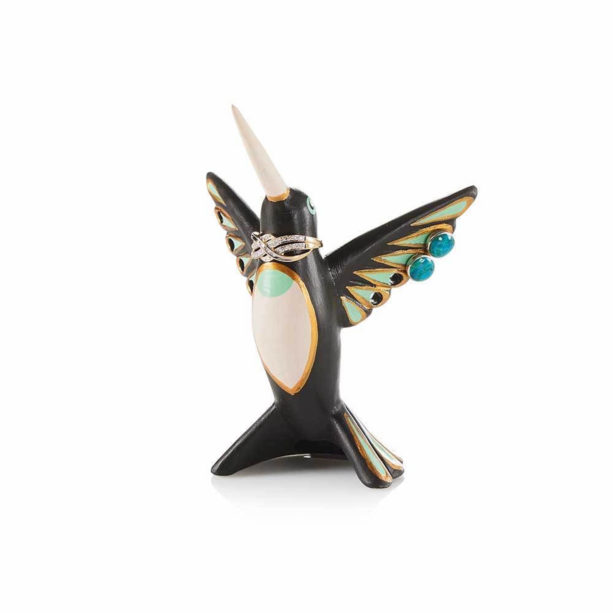 A hand-painted ceramic jewelry holder in the shape of a hummingbird holding rings and earrings.