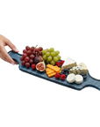 Fruit and cheese platter on a blue glass serving board held by a hand against a white background