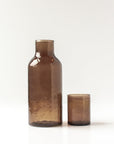 Brown hammered glass carafe and cup on a white background