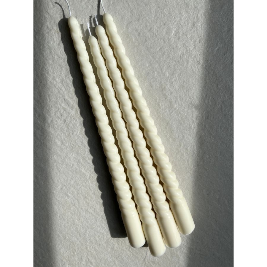 A set of two white spiral taper candles placed on a flat surface with a textured background.