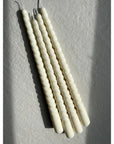 A set of two white spiral taper candles placed on a flat surface with a textured background.
