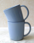 Two blue ceramic mugs, one stacked inside the other, with a half-moon handle design on a light background