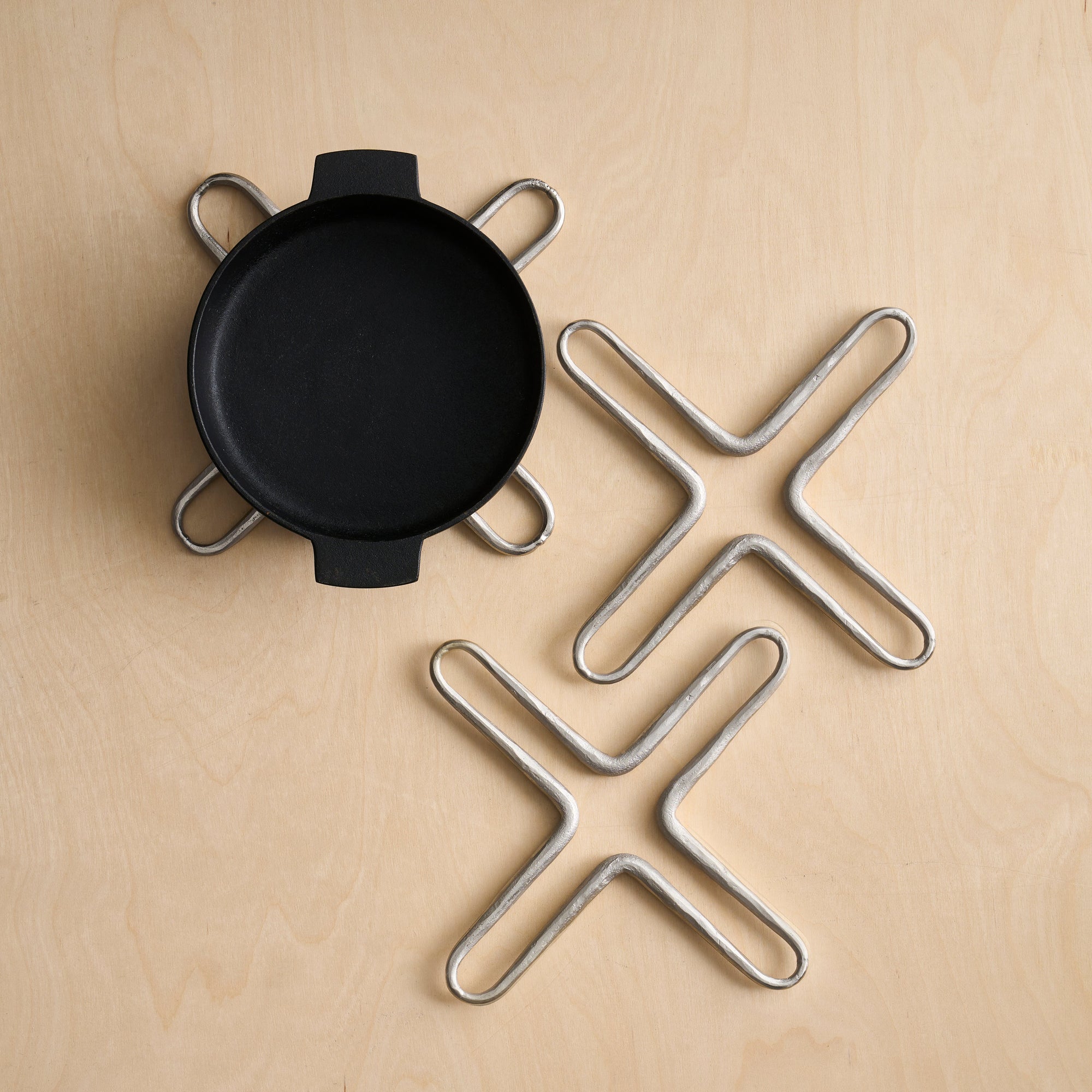 Two X-shaped pewter trivets on a wooden surface