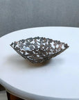 A handcrafted decorative bowl made of assorted recycled iron keys with a copper-colored finish empty on a white table.