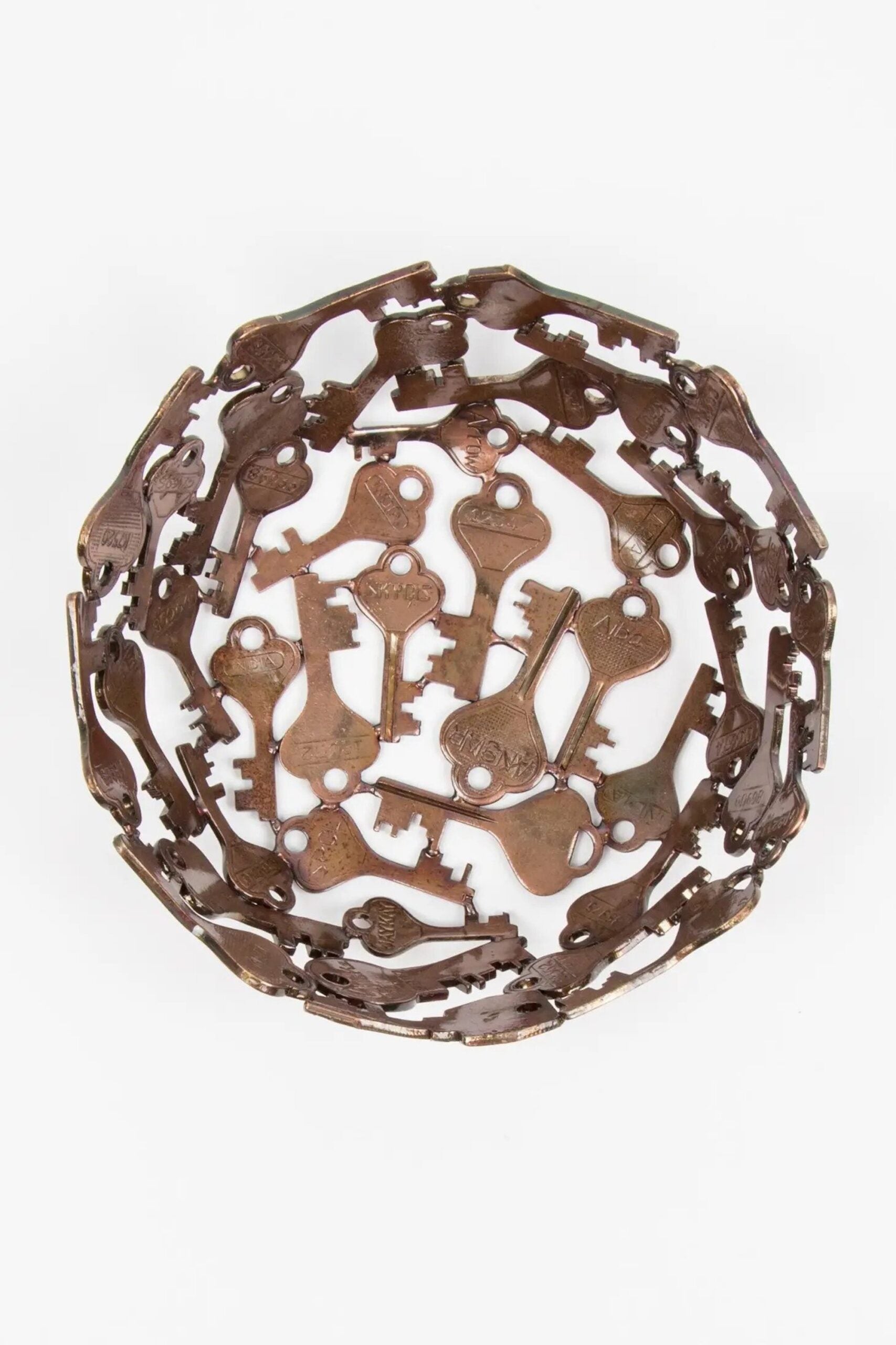 A top view of a handcrafted decorative bowl made of assorted recycled iron keys with a copper-colored finish.