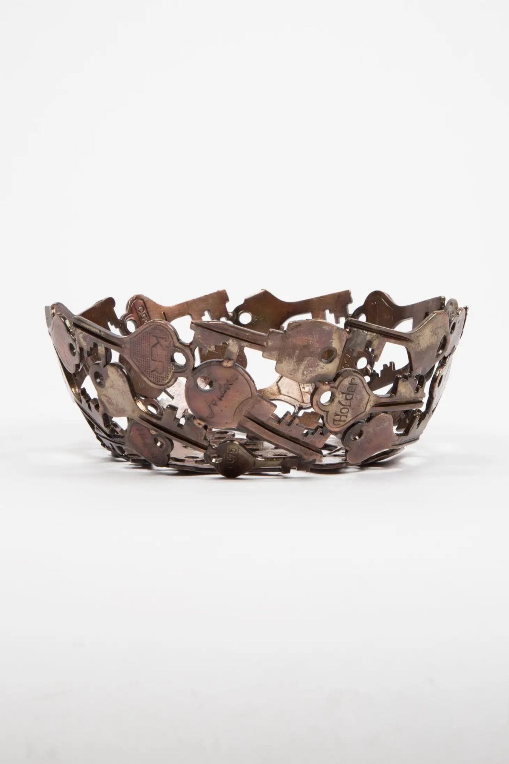 A side view of a handcrafted decorative bowl made of assorted recycled iron keys with a copper-colored finish.