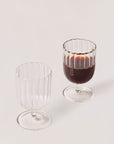 A set of two Kira stemware chalices, one empty and one filled with a dark liquid, showcasing a slender silhouette with a delicate raised liner pattern