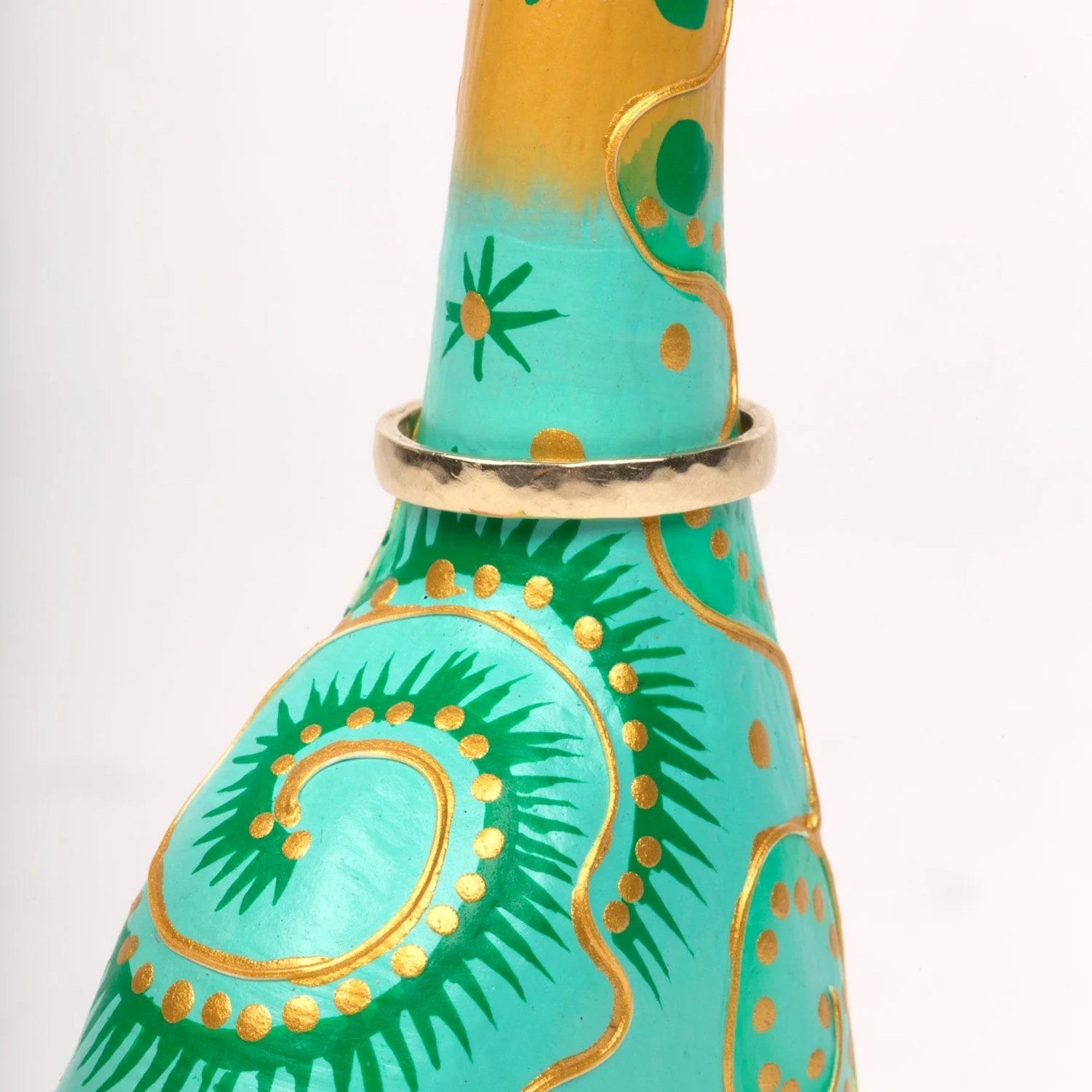 A hand-carved and hand-painted wooden ring holder in the shape of a cat with colorful patterns zoomed in on the ring.