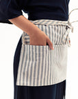 A person wearing a striped waist apron with their hand in its pockets.