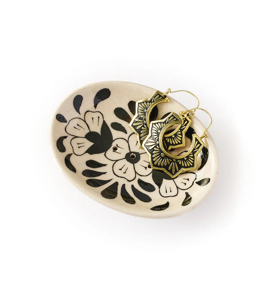 Decorative ceramic dish with black floral patterns holding gold hoop earrings on a white background