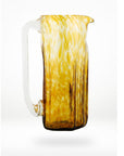 A handcrafted glass pitcher with a solid white handle and a patterned amber-colored body, indicating a molten glass technique
