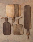 A set of four walnut wood cutting boards in varying sizes, each with a handle, against a beige background