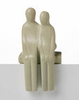 A beige stone sculpture of two figures in a standing position, intended as a shelf sitter decoration