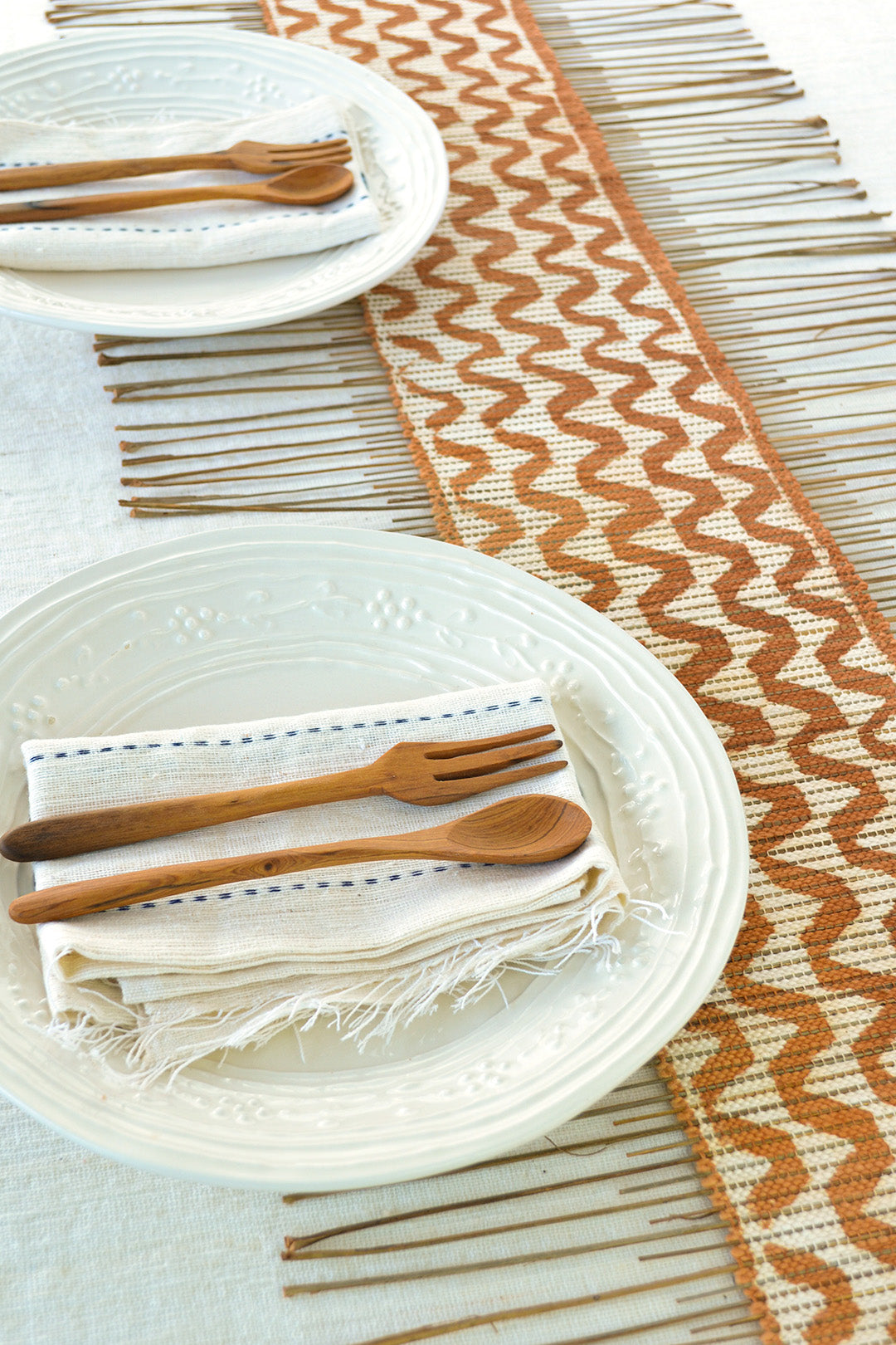 A brown and white decorative table runner with two plates napkins, and utensils on top